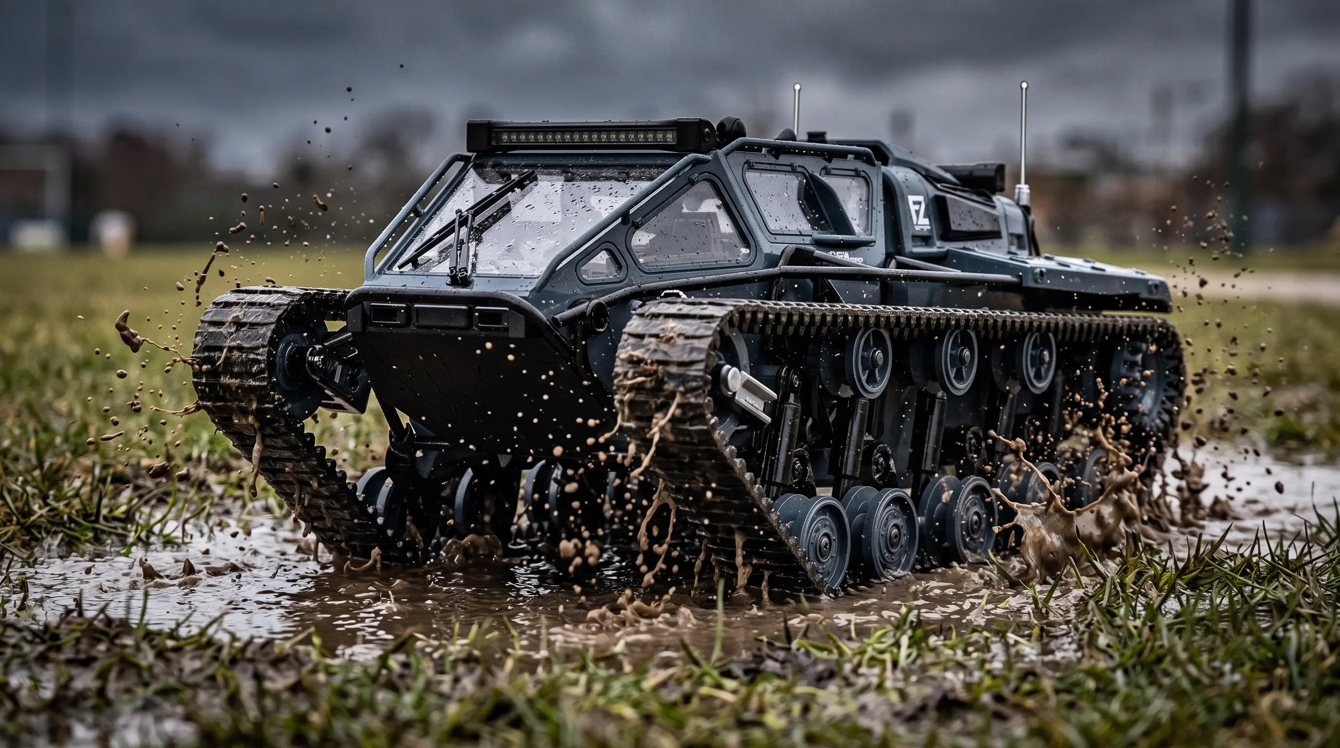 A dark grey RC tracked tank splashing through a muddy puddle on wet grass.