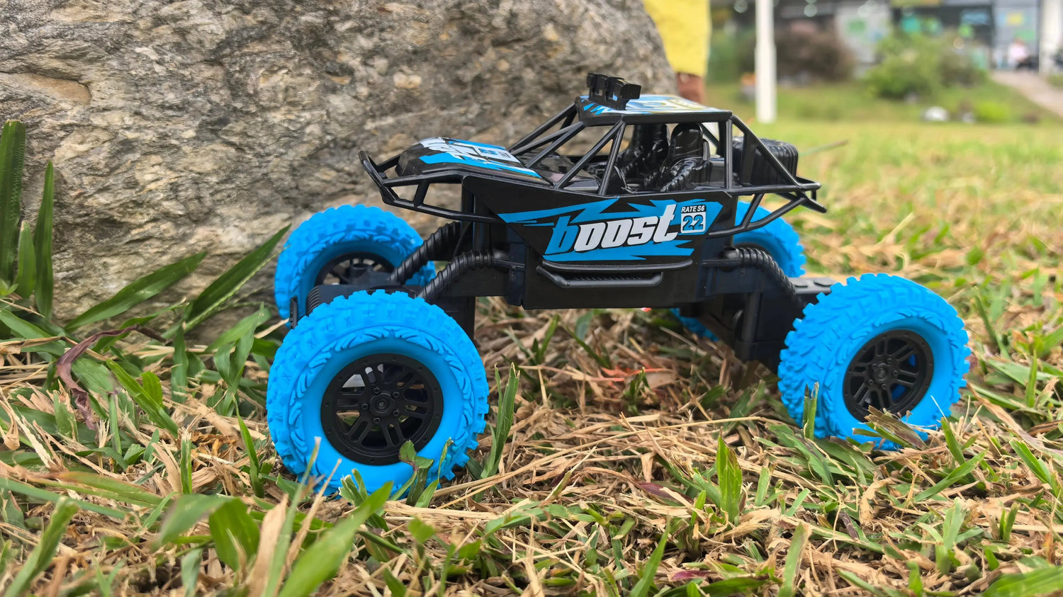 A Kids' Off-Road Truck​ toy with a black body and standout blue tires, shown in an outdoor setting on grass to demonstrate its rugged play potential.